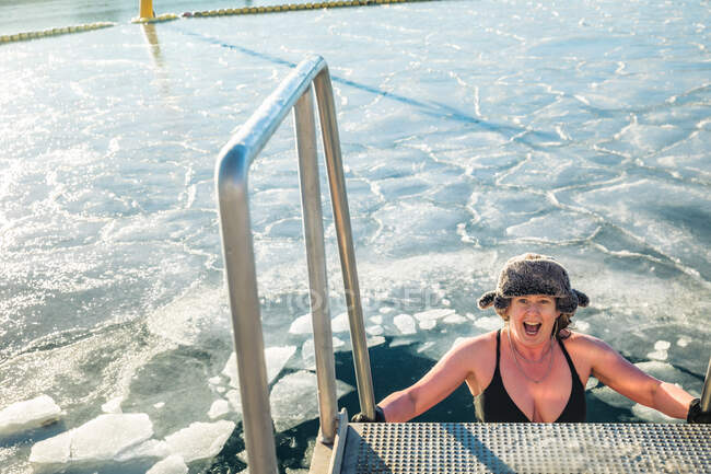 Americana mujer en piel sombrero descendente escalera a congelado agua en Dinamarca - foto de stock