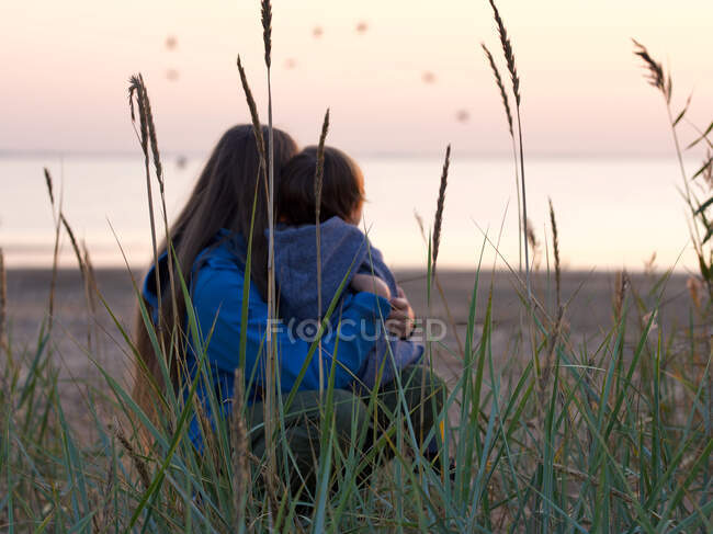 Thoughtful hugging siblings while sitting at beach, focus on cane — Stock Photo