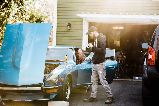Millennial hombre y padre en la ley trabajando en el viejo coche clásico juntos - foto de stock