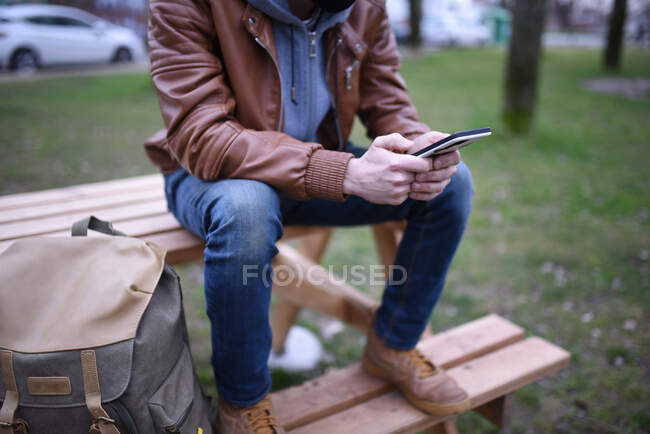 Bild zeigt die Hände eines Mannes mit seinem Mobiltelefon auf einer Holzbank in einem offenen Raum. — Stockfoto