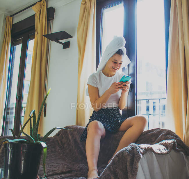 Young woman in bathrobe sitting on bed and reading book — Stock Photo