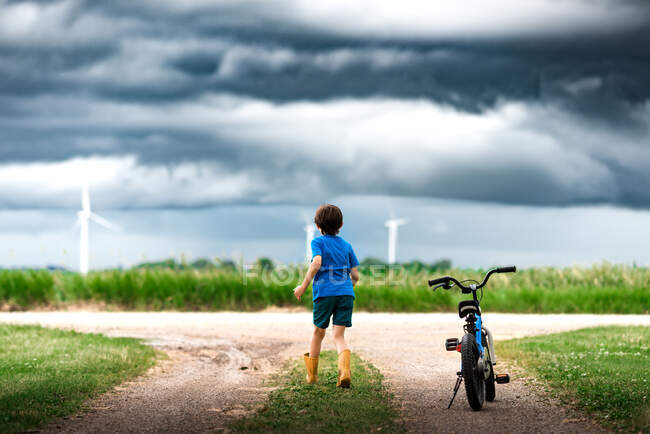 Boy with bicycle watching storm clouds over a wind farm in Iowa — Stock Photo