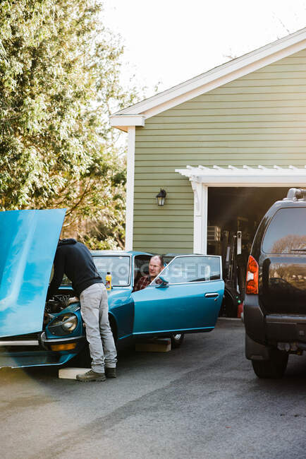 Тысячелетний мужчина и тесть вместе работают над старым классическим автомобилем — стоковое фото