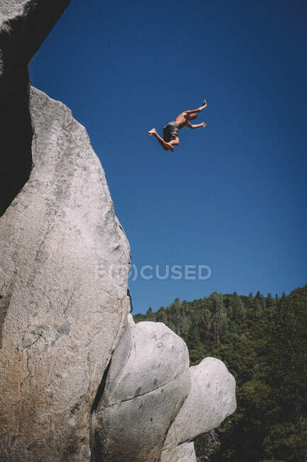 Молодой мальчик в воздухе против голубого неба после прыжка с утеса — стоковое фото