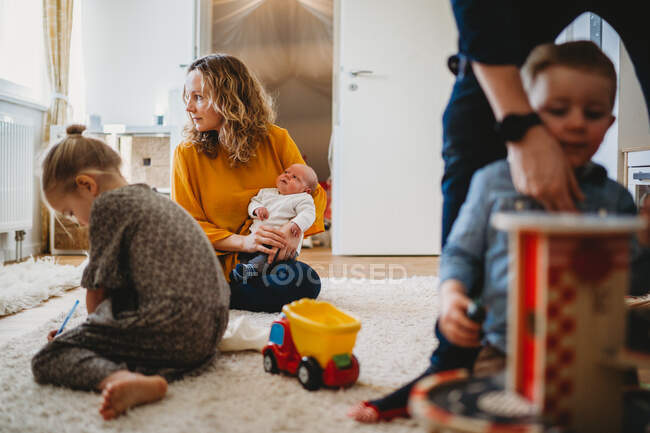 Family scene at home mom holding baby dad playing with children — Stock Photo