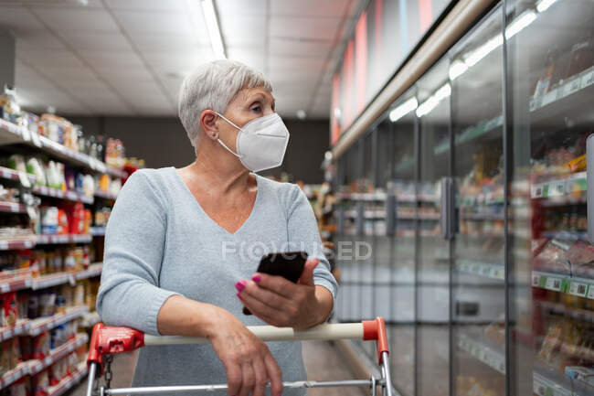 Femme âgée caucasienne avec masque facial et magasin de téléphone au supermarché — Photo de stock