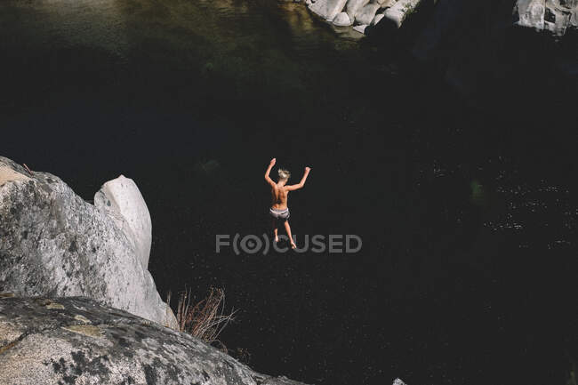 Adolescente chico saltos desde alto acantilado en oscuro piscina de agua - foto de stock
