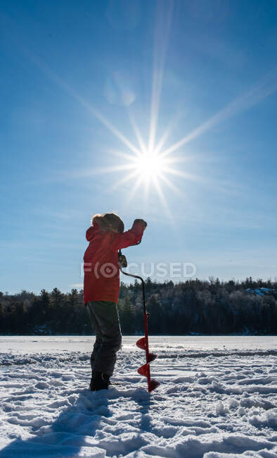 Junge benutzt Schnecke, um an einem sonnigen Wintertag ein Loch im Eis zu machen. — Stockfoto