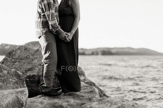 Middle aged married couple standing on rocky cliff by water — Stock Photo