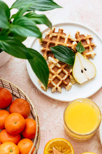 Homemade waffles on a light pink background. orange juice. fruits. — Stock Photo