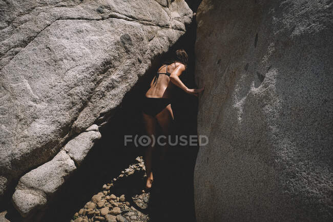 Femme en bikini jette un coup d'oeil dans une grotte sombre. Soleil et ombre — Photo de stock