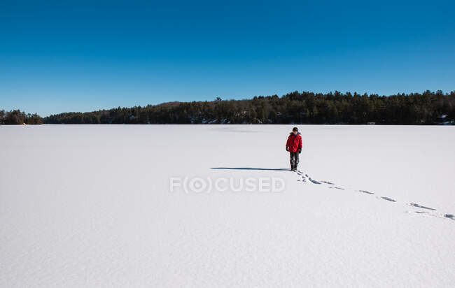 Young boy standing alone in the middle of a frozen snowy lake. — Stock Photo
