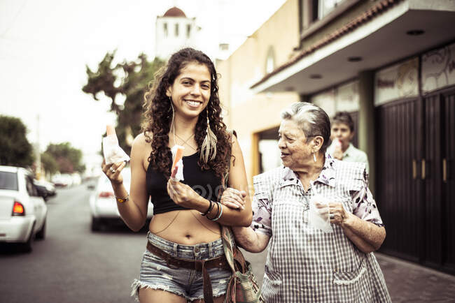 Молода приваблива мексиканка проводить свою бабусю через місцеву дорогу. — стокове фото