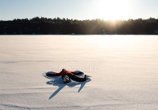 Criança fazendo um anjo de neve em um campo nevado aberto ao sol da manhã. — Fotografia de Stock