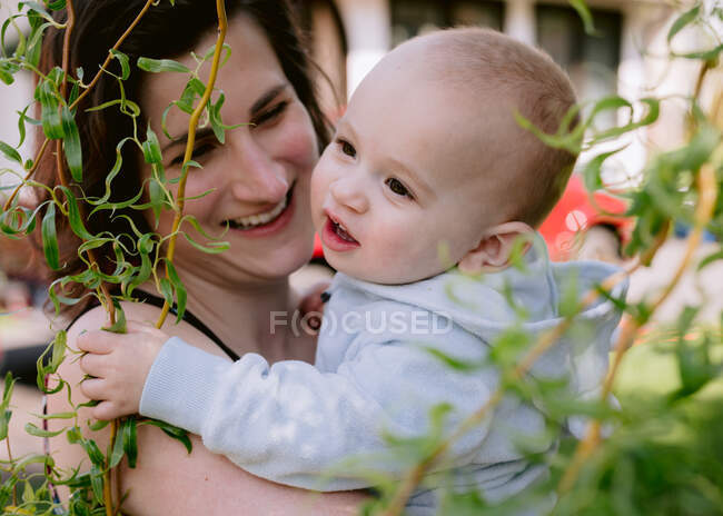 Мать и младенец смеются во дворе над плачущей ивой — стоковое фото