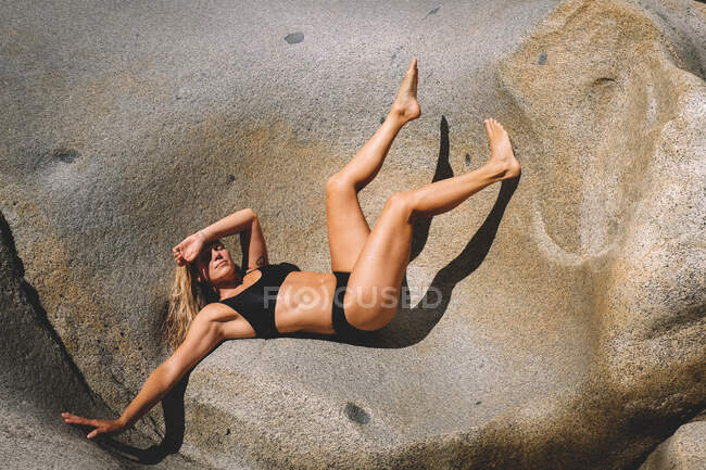 Mujer rubia posa sobre roca de granito al sol - foto de stock