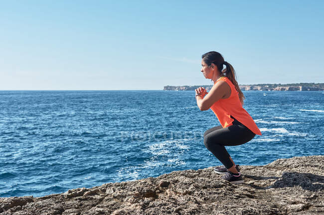 Latin woman, middle-aged, wearing sportswear, training, doing physical exercises, plank, sit-ups, climber's step, burning calories, keeping fit, outdoors by the sea, wearing headphones, smart — Stock Photo