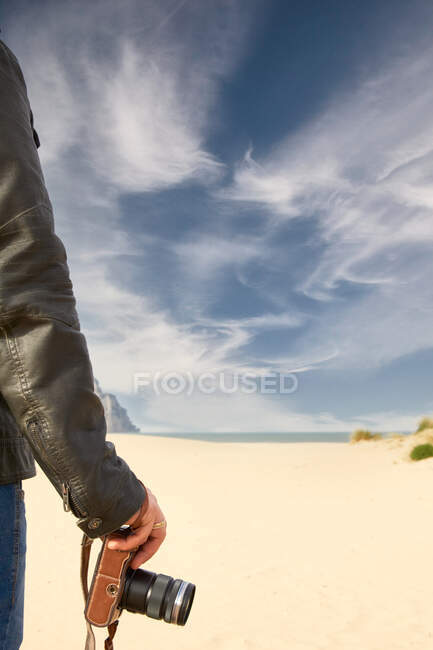 Hombre sosteniendo una cámara en la playa - foto de stock