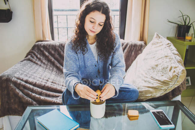 Молода жінка з печивом і кавою за сніданком сидить на дивані — стокове фото