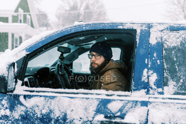 Uomo in camion nella neve guardando attraverso la finestra con occhiali e barba — Foto stock