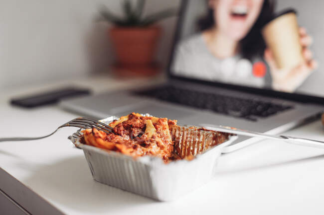 Коробка для еды с лазанью, ноутбук с видеозвонком с девушкой — стоковое фото