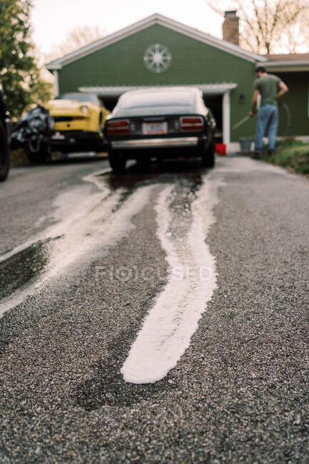 Vista de sabão suds correndo rua abaixo do homem que lava seu carro — Fotografia de Stock