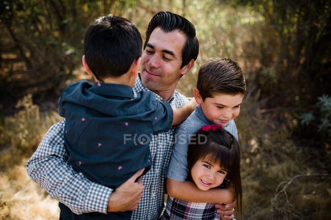 Papá sosteniendo a tres niños en el campo en San Diego - foto de stock