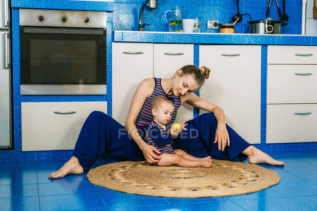 Joven mamá y su bebé jugando con manzana en la cocina - foto de stock