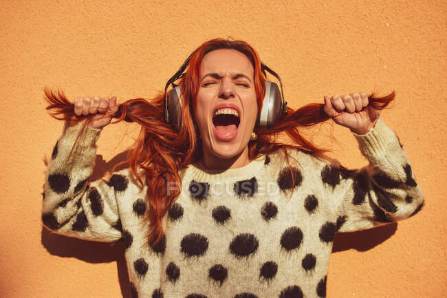 White Caucasian woman with red hair wearing helmets to protect herself from noise pulls her pigtails while screaming. Noise concept — Stock Photo