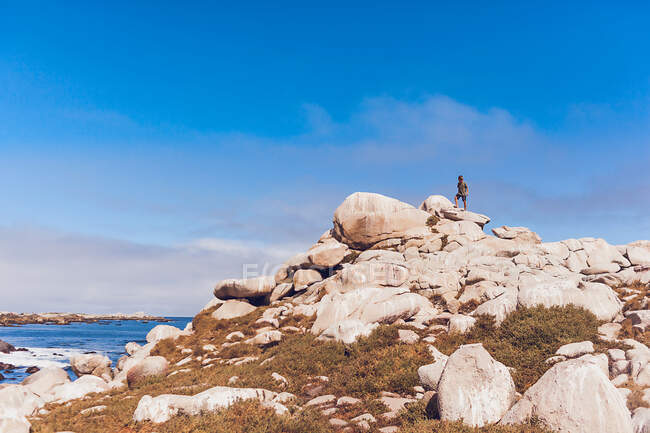 Rapaz no topo de uma montanha rochosa junto ao oceano. — Fotografia de Stock