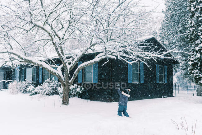 Kleines Mädchen spielt im Schnee während eines Ostersturms im Vorgarten — Stockfoto