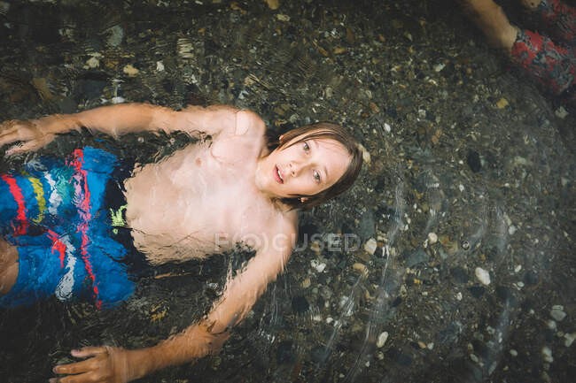 Мальчик с зелеными глазами лежит на мелководье в летнюю жару — стоковое фото
