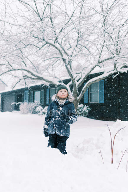 Little boy standing in the snow in front of ranch house in nor'easter — Stock Photo