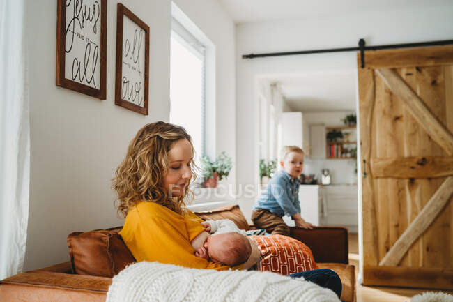 Mãe amamentando bebê recém-nascido em casa em sala de família com filho — Fotografia de Stock