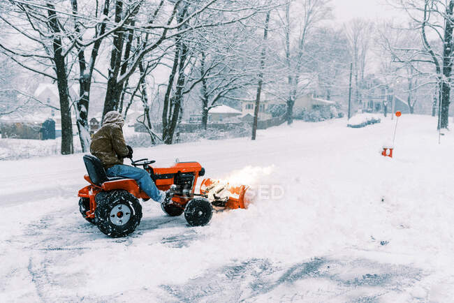 Homme sur un tracteur labourant de la neige dans une allée pendant une tempête de nord-est — Photo de stock