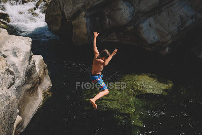 Menino salta de Boulder para a água preta e verde do rio — Fotografia de Stock
