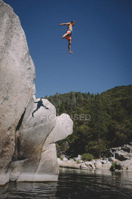 Giovane ragazzo Mid Air contro il cielo blu dopo aver saltato da una scogliera — Foto stock