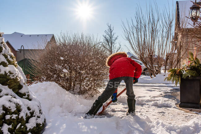 Мальчик в красном пальто убирает снег с дорожки своего дома. — стоковое фото
