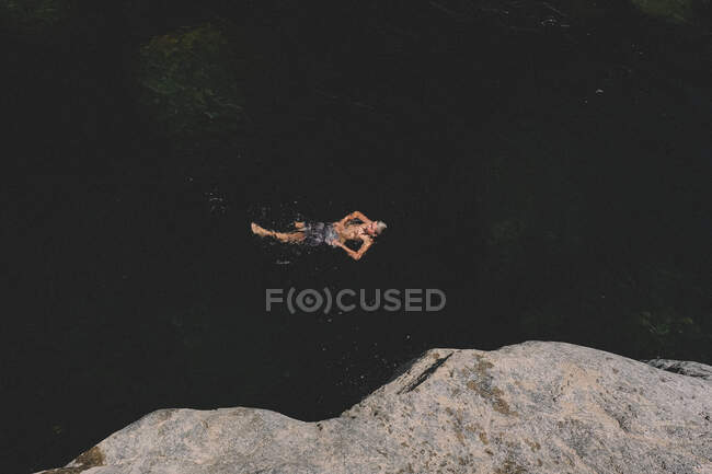 Взгляд с высоты птичьего полета на мальчика, плывущего спиной в темной воде — стоковое фото