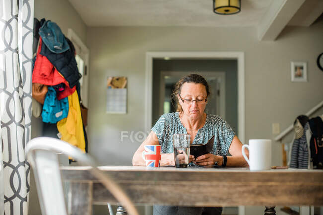 Mulher de meia idade olhando em seu telefone inteligente e tomando café — Fotografia de Stock