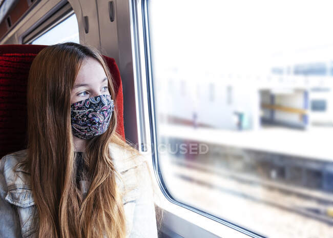 Молодий підліток виглядає стурбованим подорожами на поїзді в масці — стокове фото