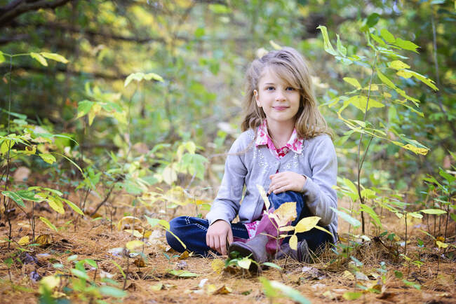 Jovencita rubia sentada en el suelo en el bosque. - foto de stock