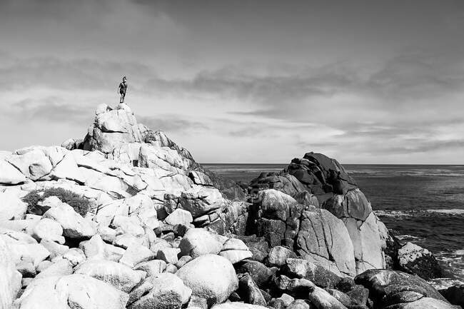 Foto em preto e branco de um menino no topo ou uma montanha rochosa junto ao oceano — Fotografia de Stock