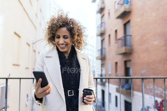 Hermosa mujer en la ciudad con café y teléfono inteligente - foto de stock