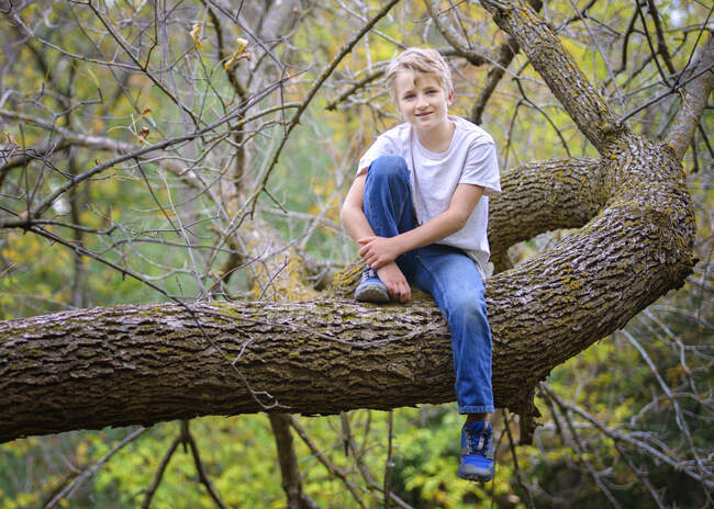 Jovem loiro feliz ao ar livre sentado em uma árvore. — Fotografia de Stock