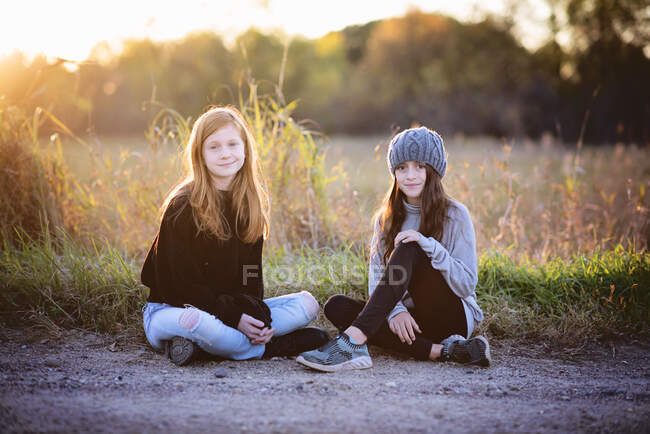 Two beautiful young tween girls sitting outdoors in fall, backlit. — Stock Photo