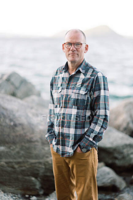 Мужчина средних лет, стоящий у скалистого пляжа в Новой Англии, улыбаясь — стоковое фото