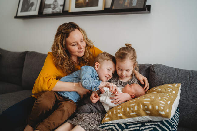 Schöne liebevolle Mutter und Kinder, die ihr Neugeborenes zu Hause halten — Stockfoto