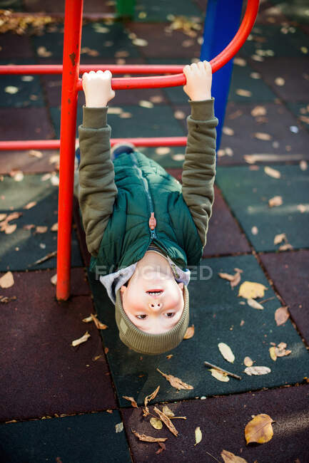 Niedliches Kind hängt kopfüber an Affenstangen auf Herbstspielplatz — Stockfoto