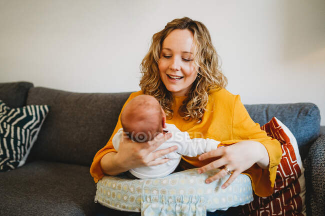 Glückliche Mutter schaut auf ihr neugeborenes Baby, das zu Hause auf der Couch sitzt — Stockfoto